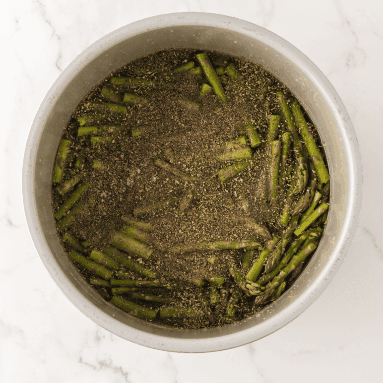 Asparagus stalks, savory spices, and golden chicken broth being added to the Ninja Foodi inner pot before pressure cooking.