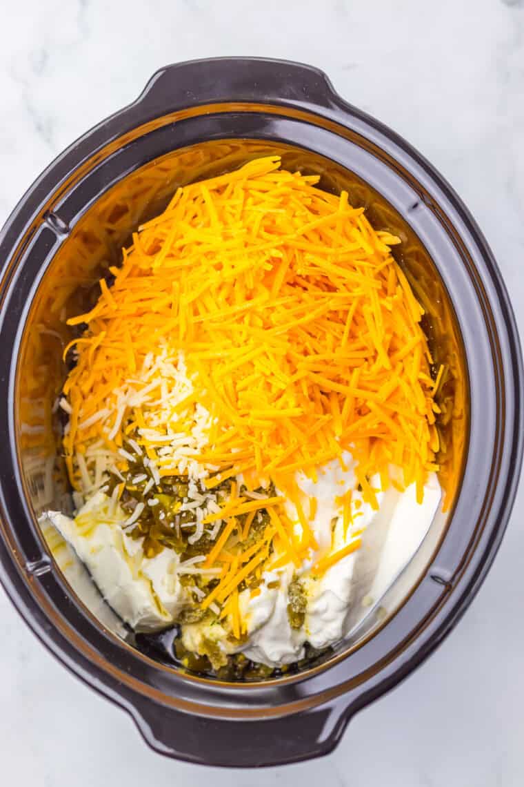 Slow cooker filled with cream cheese, sour cream, cheeses, and jalapeños