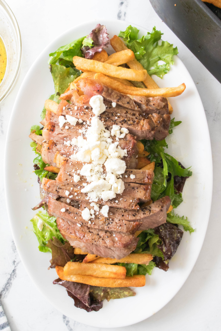 Air fryer-cooked steak served with crispy golden fries, garnished with fresh herbs on a plate.