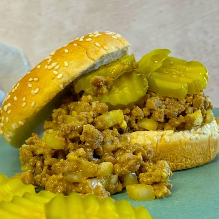 Air fryer copycat Maid-Rite sandwich with seasoned ground beef on a soft bun, served on a plate with a side of pickles.