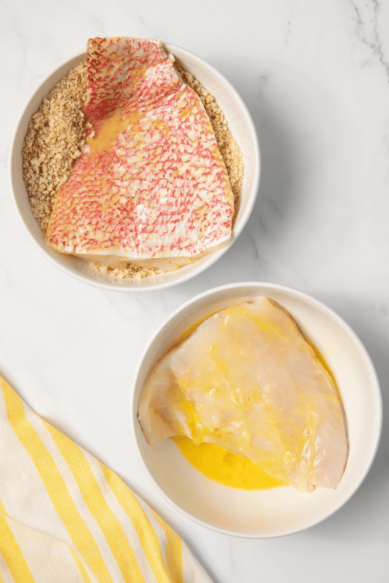 Red snapper fillets being patted dry with paper towels on cutting board