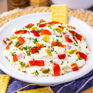 Creamy cream cheese pepper dip served in a bowl with crackers and fresh vegetables on the side.