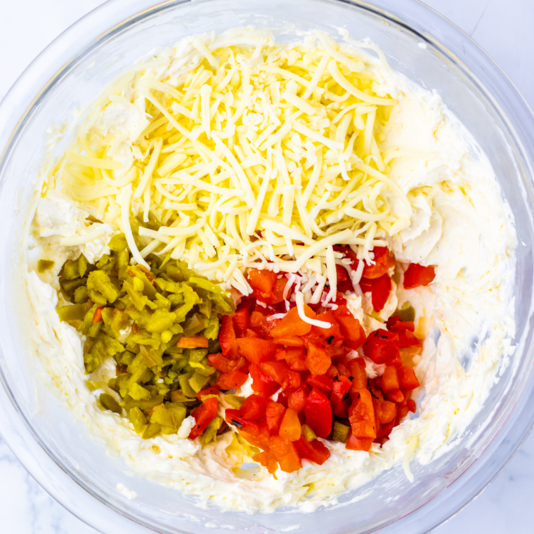 Cream cheese dip mixture with diced red peppers, jalapeños, and shredded cheese in a bowl, ready to chill.