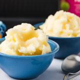 Scoop of creamy homemade lemon gelato made in the Ninja Creami, served in a bowl with fresh lemon slices.