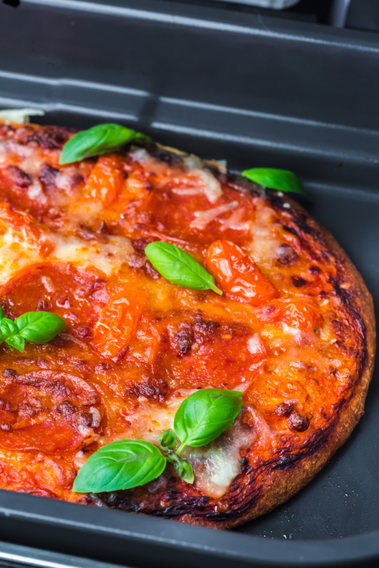 Freshly baked Ninja Woodfire pizza with golden crust, melted cheese, and assorted toppings on a cutting board.