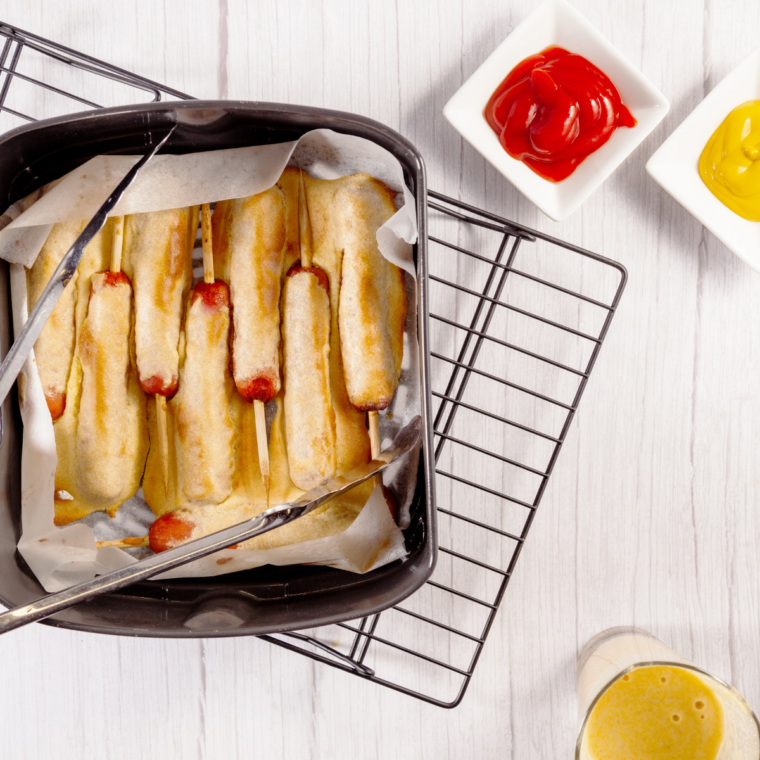 Air fryer corn dogs with crispy cornbread coating and wooden skewers on a serving plate.