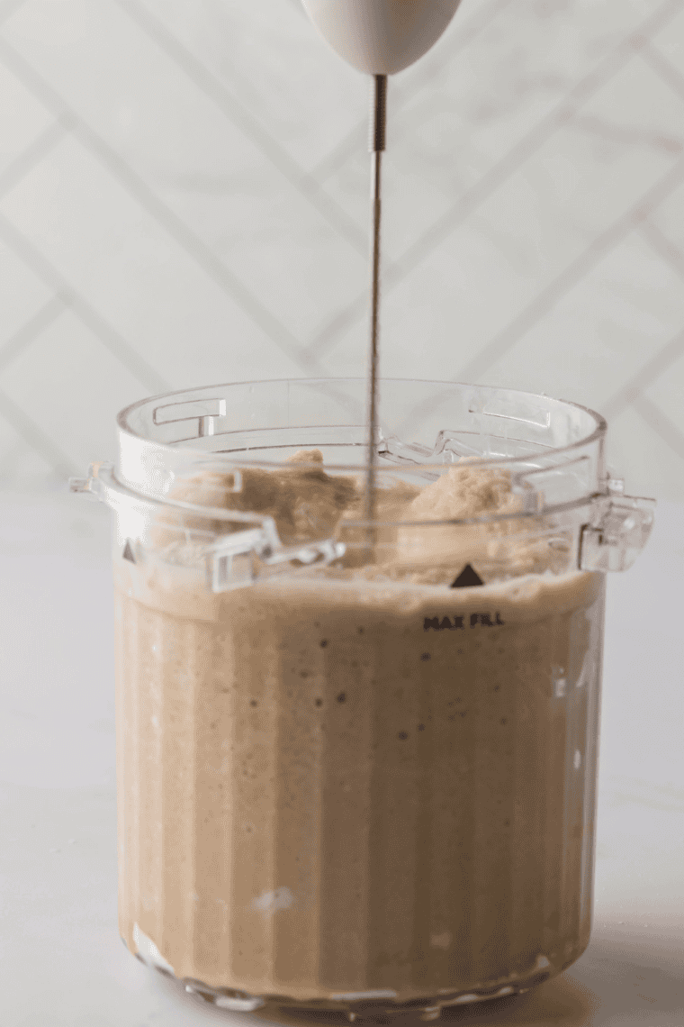 Pouring White Chocolate Mocha Frappuccino® mixture into a Ninja Creami pint, folding in white chocolate chips.