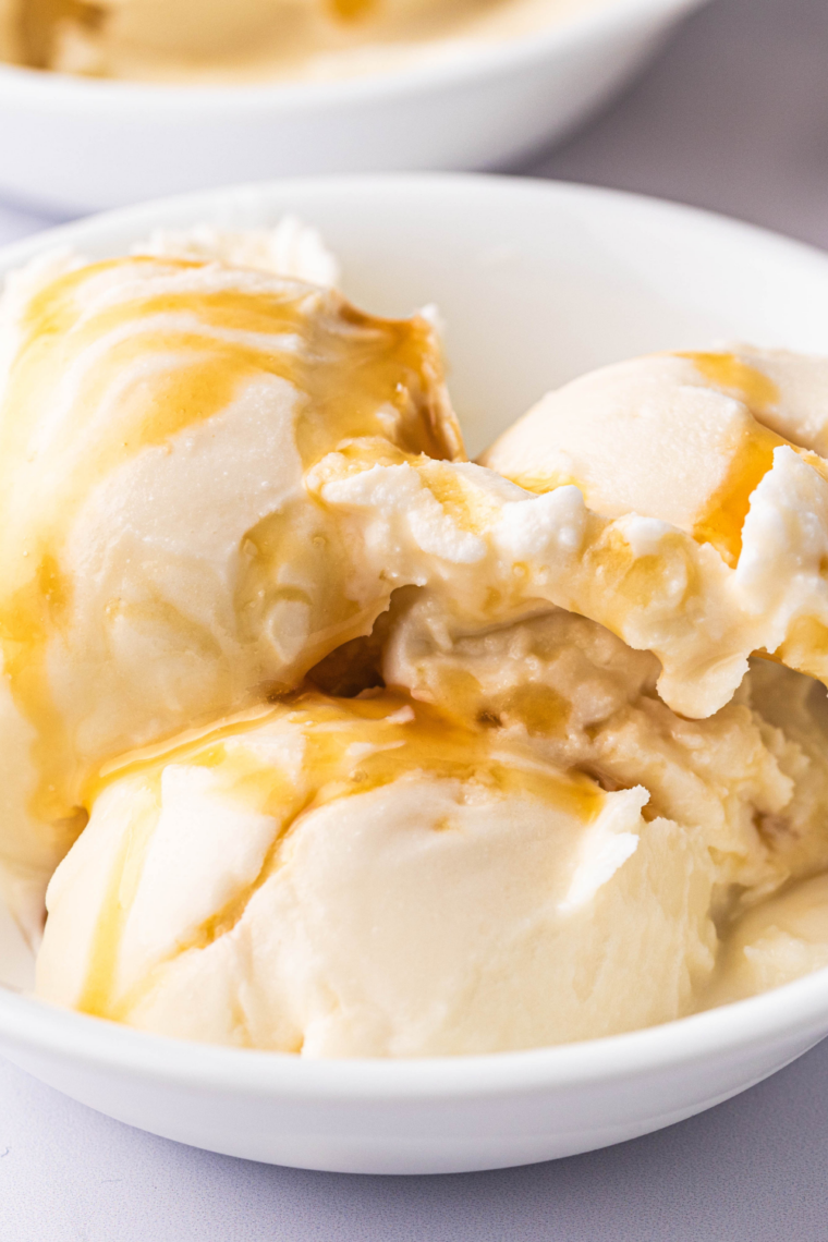 A close-up, top-down view of a smooth and creamy bowl of Salted Caramel Gelato made in a Ninja Creami, featuring a rich, golden-amber hue and a glossy, dense texture. The gelato is topped with a drizzle of decadent caramel sauce and a light sprinkle of flaky sea salt, served in a ceramic bowl that highlights its professional, artisanal finish.