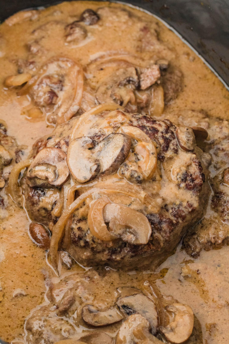 Slow Cooker Salisbury steak smothered in creamy mushroom sauce, served on a plate with mashed potatoes and garnished with parsley.