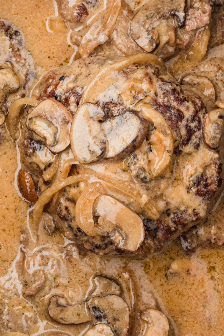 Tender Salisbury steak patties smothered in creamy mushroom sauce, served on a plate with mashed potatoes and garnished with fresh parsley.