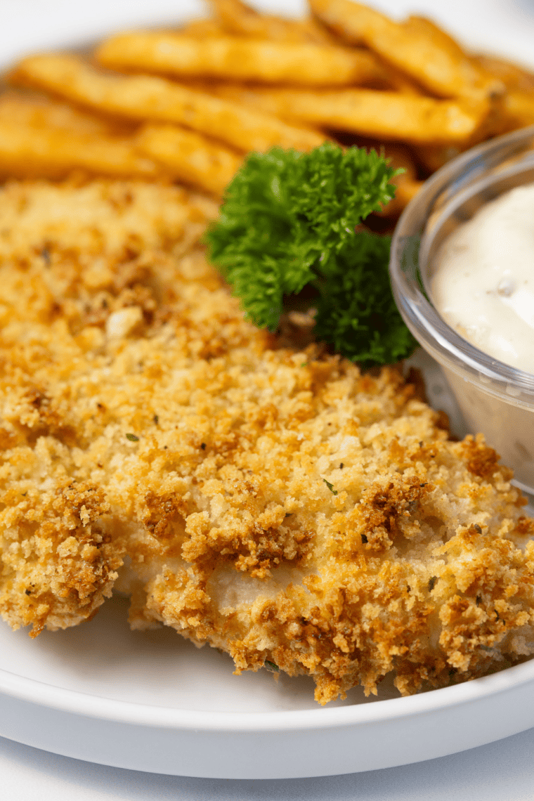 Golden, crispy panko air fryer haddock served on a plate with lemon wedges and garnish.