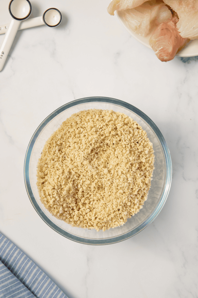 Haddock fillet being dredged in flour, dipped in egg mixture, then coated with panko breadcrumbs.
