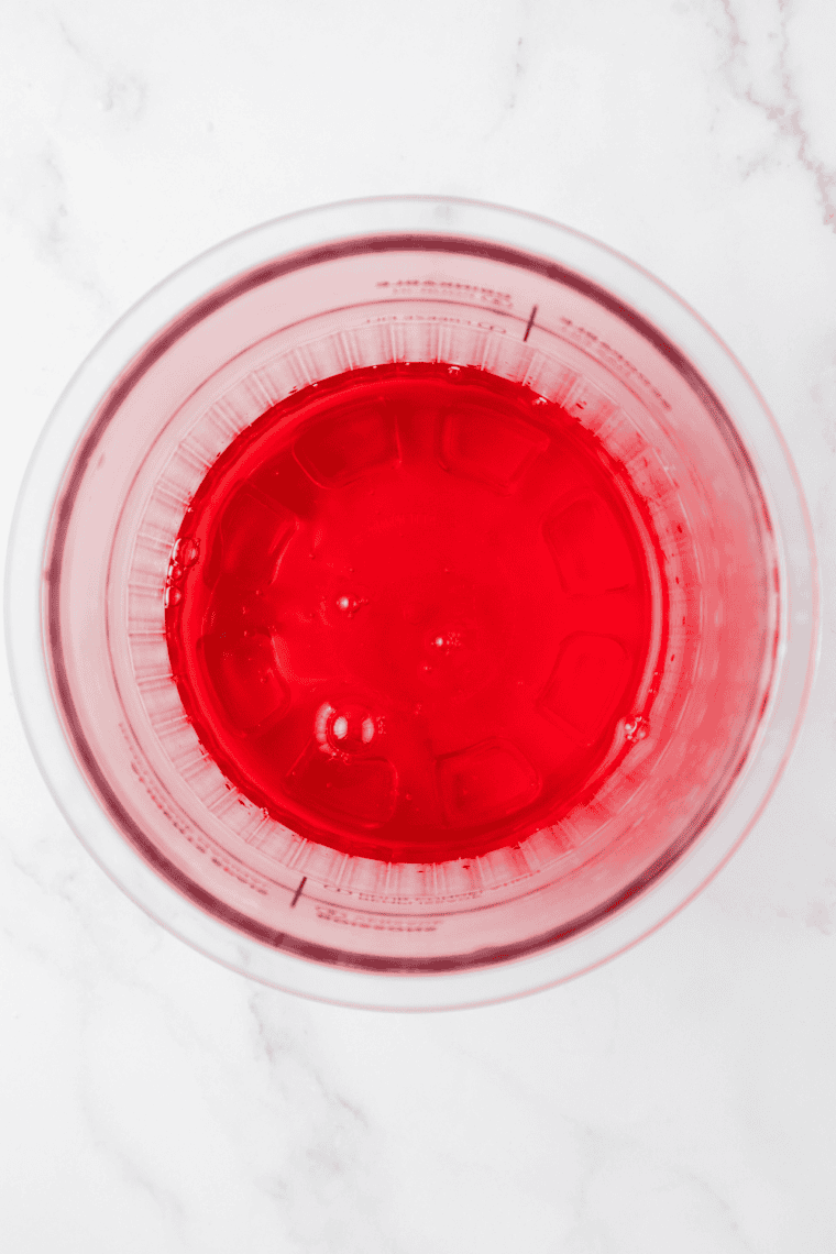Cherry syrup and water being stirred together in a mixing bowl.