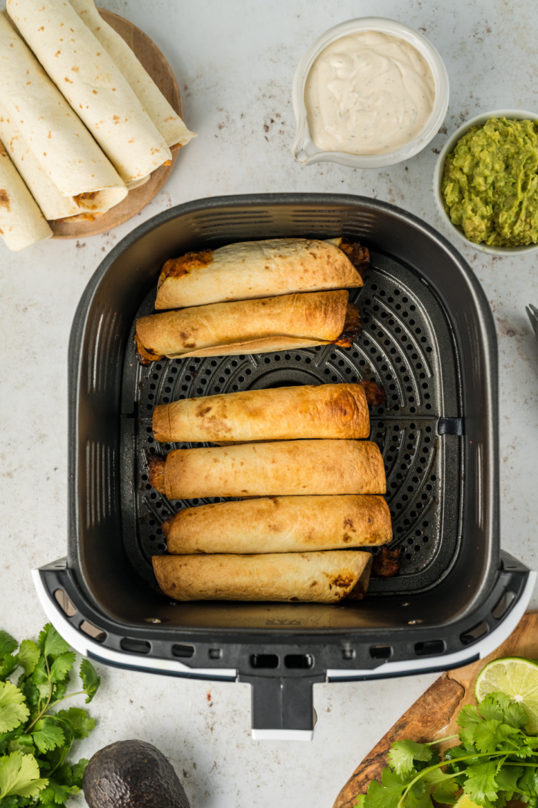 Taquitos arranged in air fryer basket with space between each for airflow.