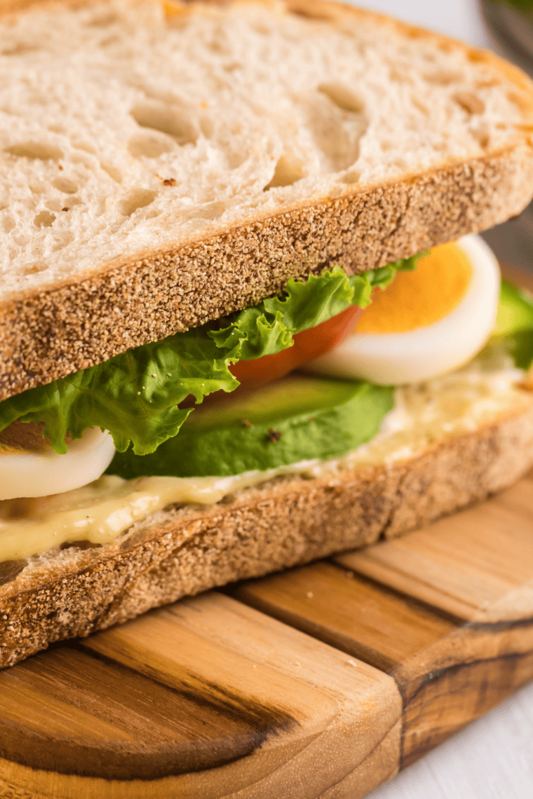 Close-up of a BLTE sandwich with crispy bacon, lettuce, tomato, and a fried egg stacked on toasted bread served on a plate.