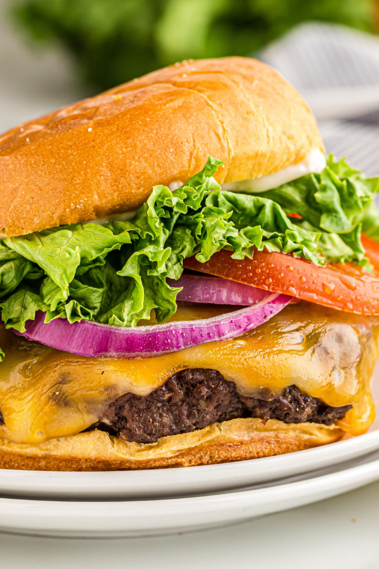Close-up of smash bacon cheeseburger in cast iron skillet with sizzling beef, melted cheese, and crispy bacon strips.