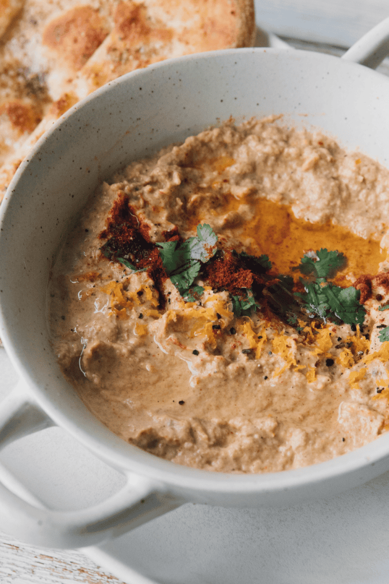 Creamy roasted eggplant dip topped with olive oil and herbs served with pita bread and vegetables