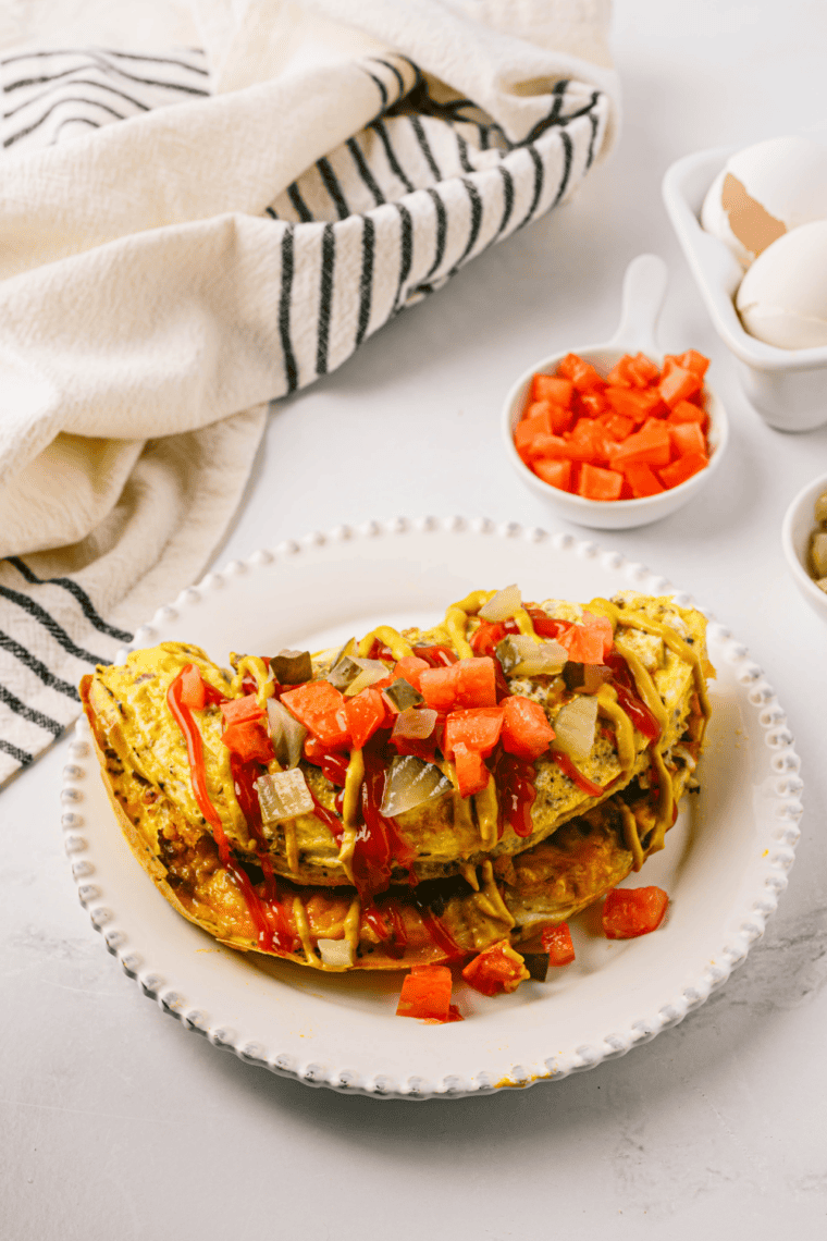 Easy First Watch The Works Omelet filled with bacon, ham, sausage, vegetables, and melted cheese on a plate