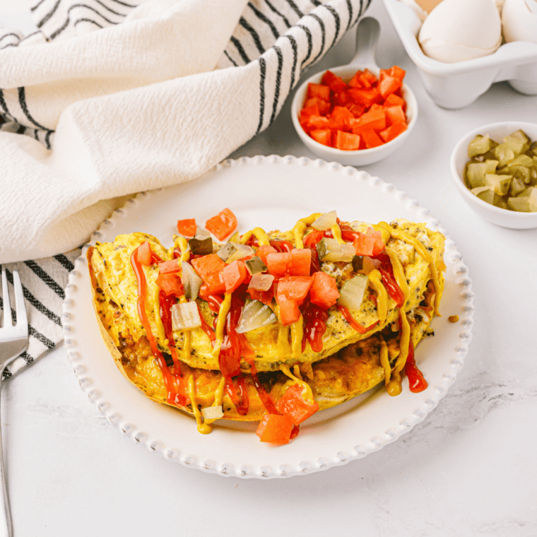 Loaded First Watch The Works Omelet with eggs, bacon, ham, sausage, peppers, onions, mushrooms, and melted cheese on a plate