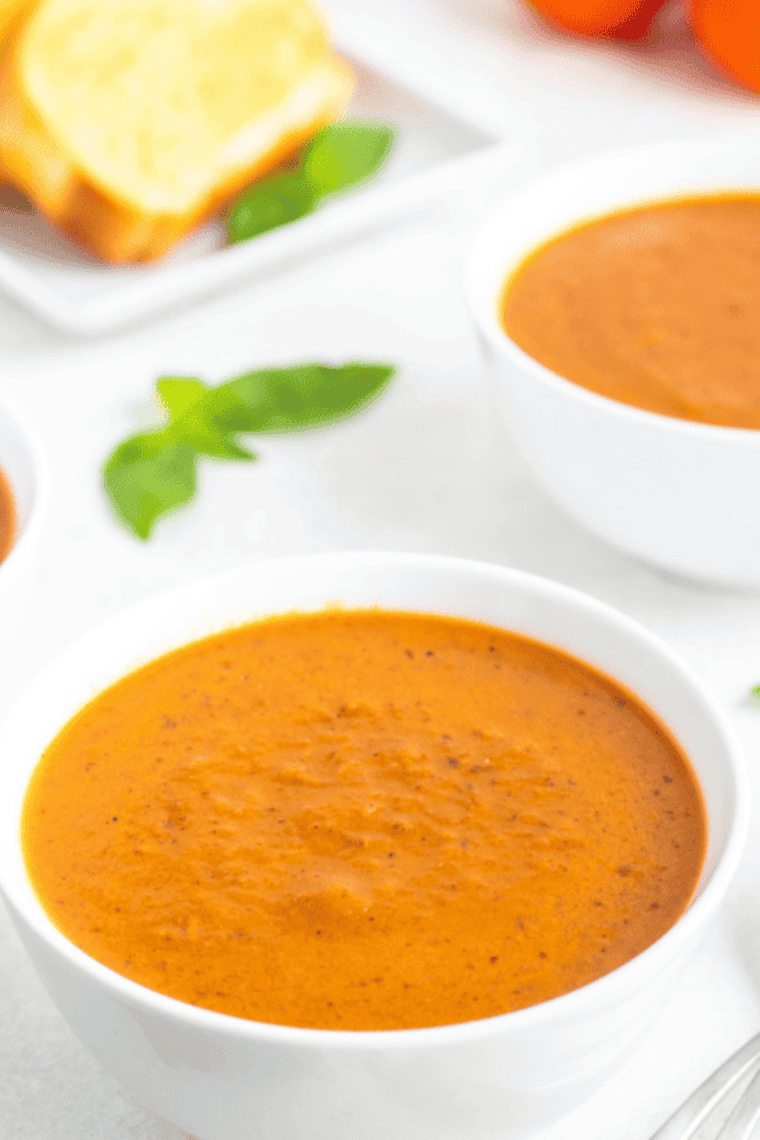 Bowl of creamy tomato basil soup garnished with fresh basil and a drizzle of cream, served with crusty bread on the side.