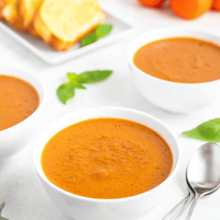 Bowl of creamy tomato basil soup garnished with fresh basil leaves and a drizzle of cream.