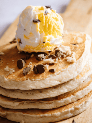Stack of fluffy chocolate chip pancakes topped with melting chocolate chips and syrup on a white plate styled like First Watch breakfast presentation.