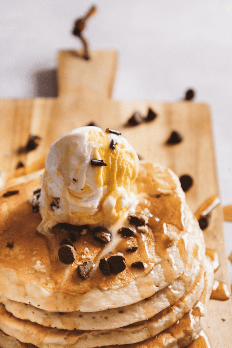 Stack of fluffy chocolate chip pancakes topped with melting chocolate chips, syrup, and butter served on a white plate in classic brunch style.