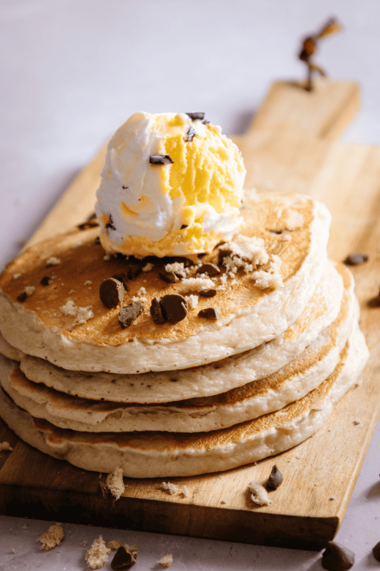 Stack of fluffy chocolate chip pancakes topped with melted chocolate chips and syrup served on a white plate with a classic breakfast style presentation.
