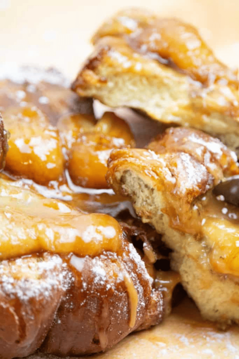 Golden Floridian French toast made with brioche bread topped with powdered sugar, fresh berries, bananas, and maple syrup on a white brunch plate.