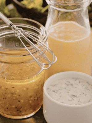 Creamy homemade lemon dressing in a glass jar with fresh lemon juice, olive oil, and herbs, served alongside a fresh green salad.