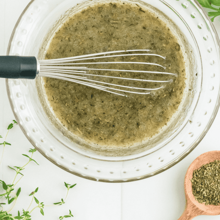 Whisking vinegar mustard garlic herbs salt pepper mixture.