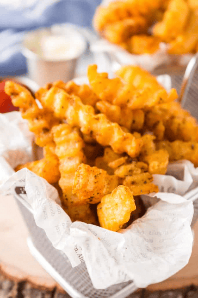Small bowl of homemade French fry seasoning spice blend next to crispy golden fries on a wooden table.