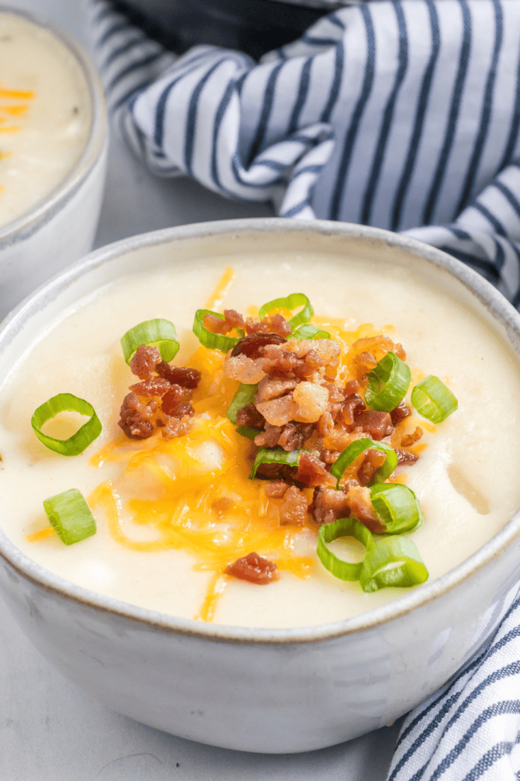 Bowl of creamy McAlister’s potato soup topped with crispy bacon, shredded cheddar cheese, and green onions rich copycat loaded baked potato soup.