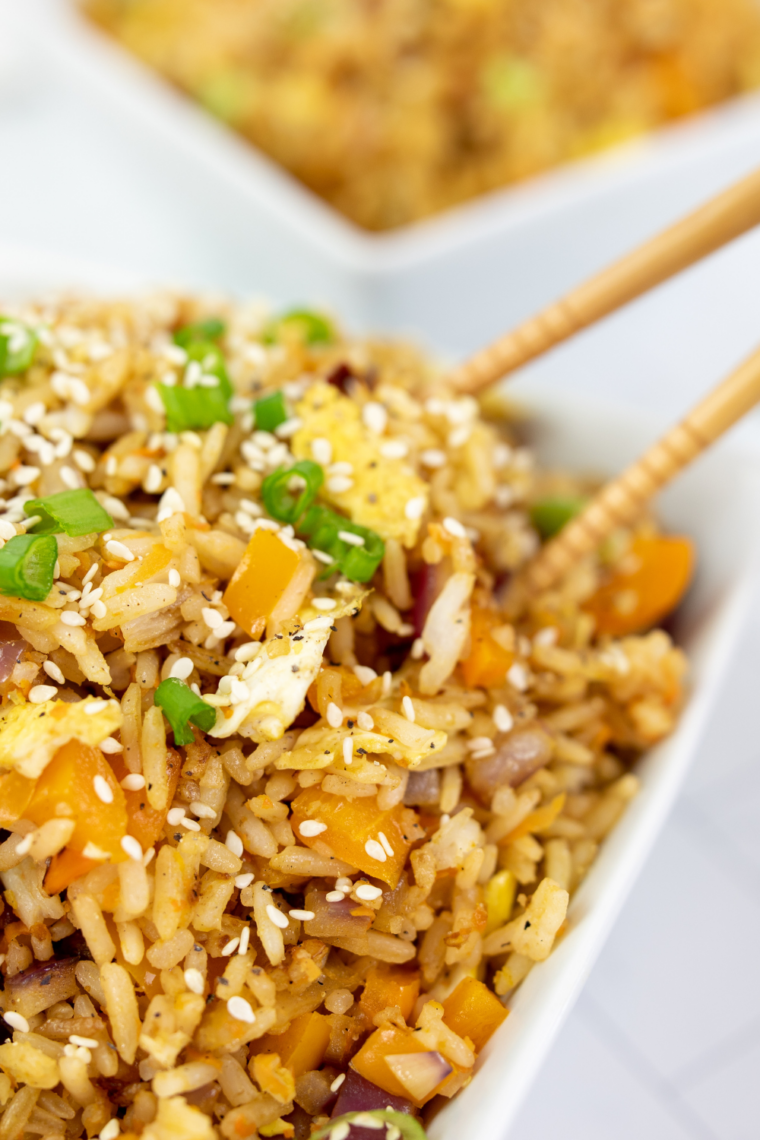 Close up of fried rice on a Blackstone griddle with scrambled eggs, peas, carrots, and soy sauce being mixed together with spatulas.