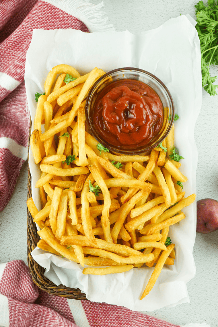 Small bowl of Zaxby’s fry seasoning next to crispy golden fries being sprinkled with spice blend for extra flavor.