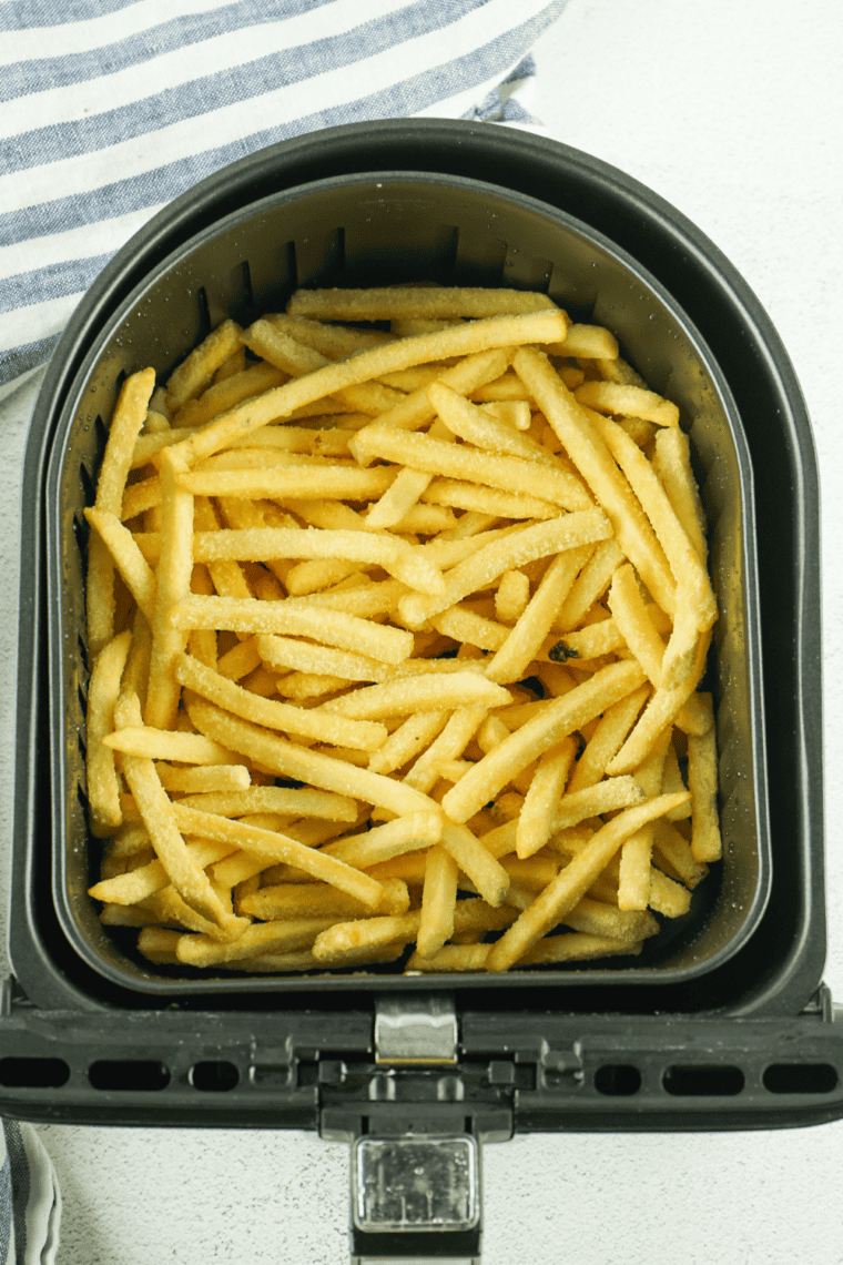 Small bowl of Zaxby’s fry seasoning spice blend next to crispy golden fries being seasoned for extra flavor.