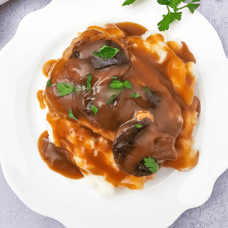 Close-up of crock pot pork chops in thick creamy sauce with onions and gravy.