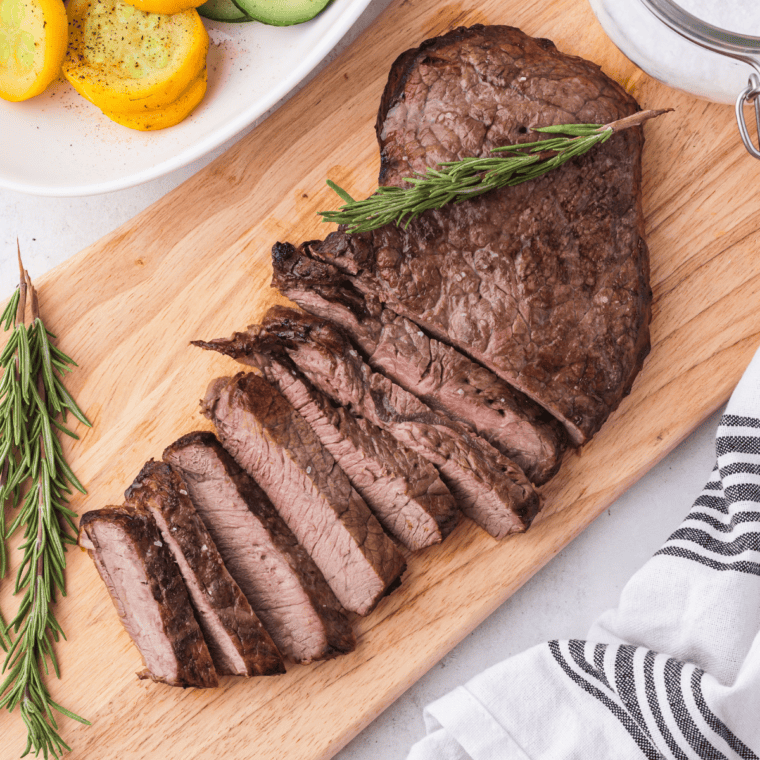 Juicy air fryer round steak sliced on a cutting board with garlic butter and herbs.