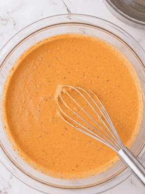 Copycat Burger King Buffalo Sauce in a glass mason jar with a spoon lifting creamy orange sauce