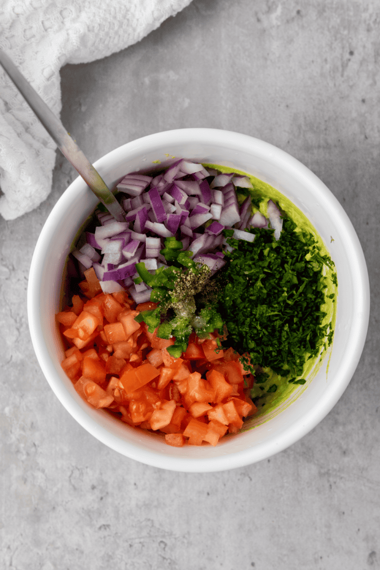 Folding diced red onion, jalapeño, cilantro, and Roma tomatoes into mashed avocado for copycat Chipotle guacamole
