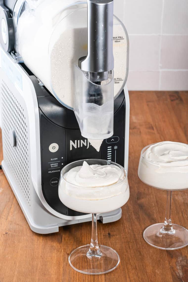 Frozen Brandy Alexander being poured into coupe glass topped with whipped cream and nutmeg garnish