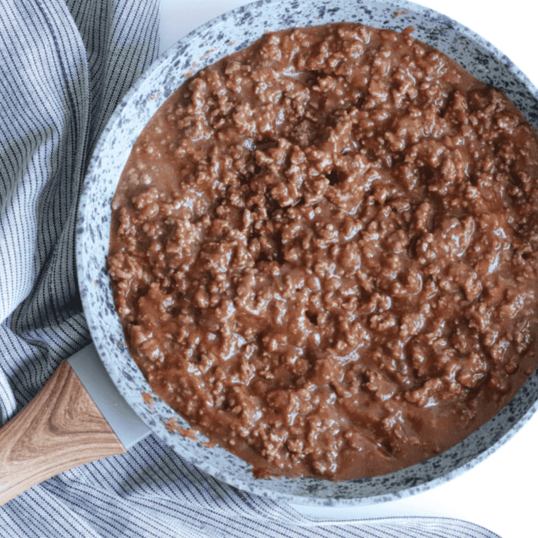Ground beef browning in a large skillet over medium-high heat, being broken apart with a wooden spoon, with diced onion and bell pepper cooking alongside until tender and fully combined.