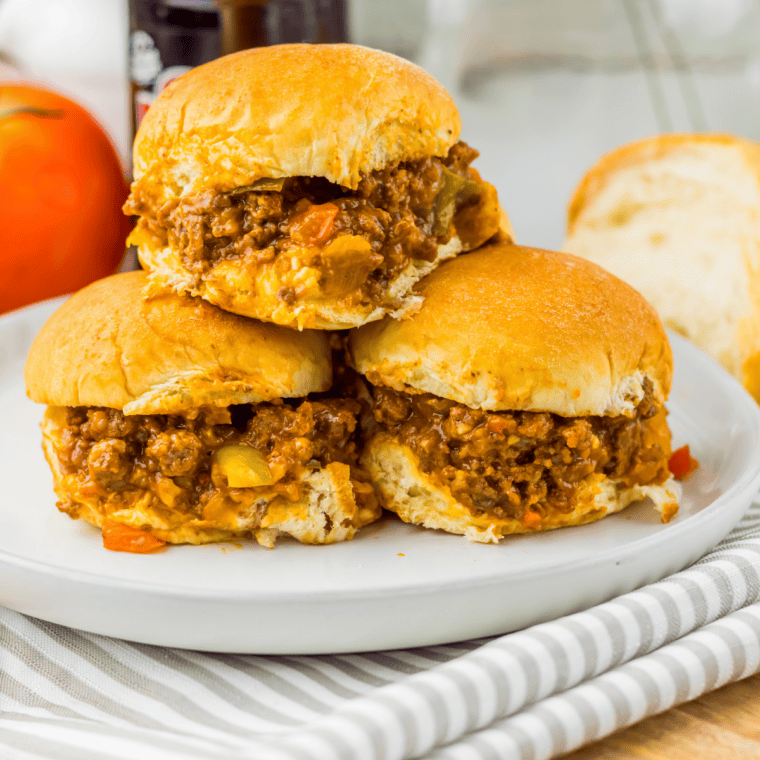 Wooden spoon stirring Sloppy Joe filling in a skillet with ground beef and tomato sauce.