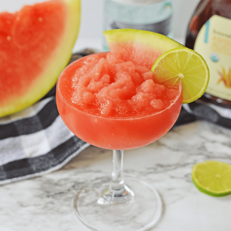 Bright pink watermelon daiquiri slush served in a glass with ice crystals and a watermelon wedge.