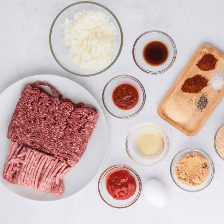 One pound meatloaf ingredients laid out: ground beef, breadcrumbs, milk, egg, diced onion, garlic, Worcestershire, Dijon, seasonings, ketchup, and brown sugar for the glaze.