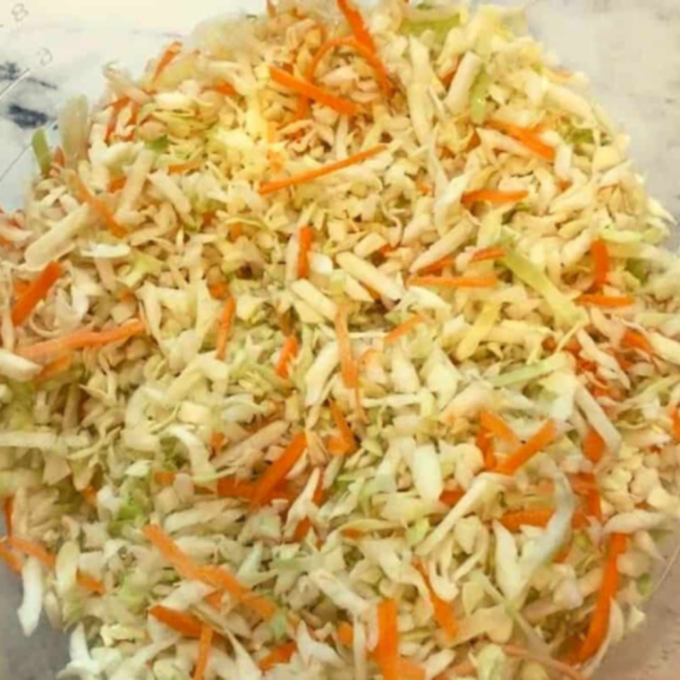 Finely sliced cabbage and grated carrots being prepped on a cutting board for homemade Popeyes-style coleslaw recipe