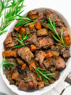 Homemade pot roast seasoning blend in a small bowl with dried herbs and spices on a wooden table.