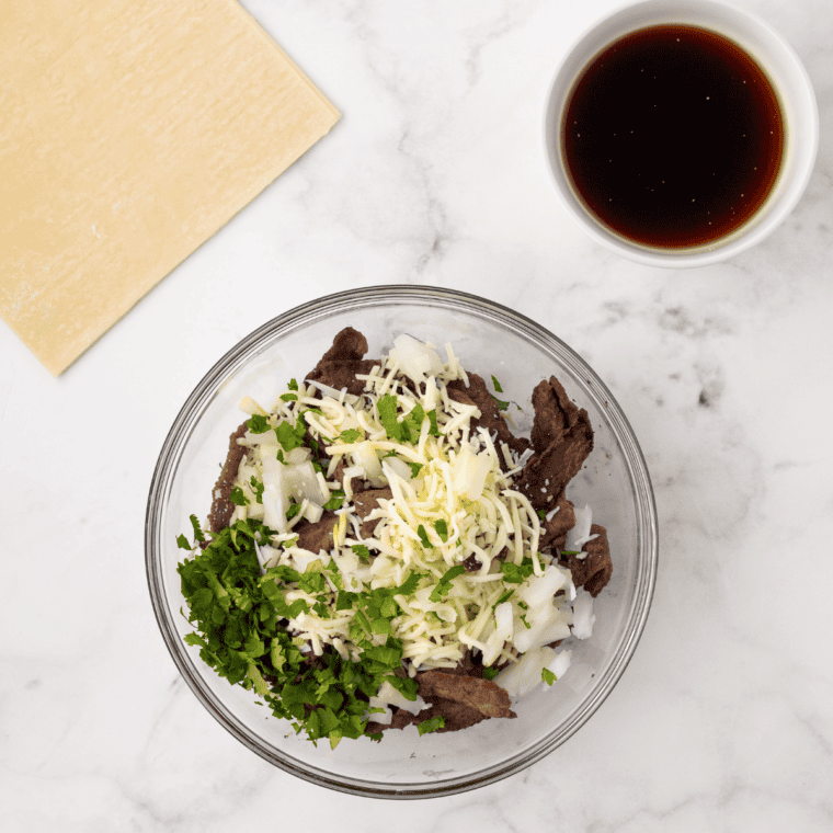 Shredded birria beef draining in a strainer over reserved consommé
