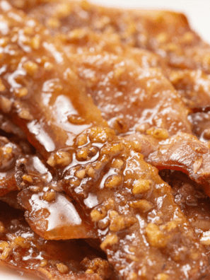 Air fryer praline bacon strips coated in caramelized brown sugar and chopped pecans on parchment paper