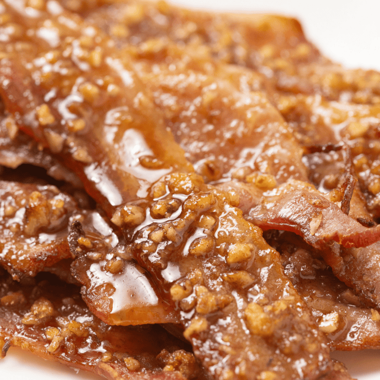 Air fryer praline bacon strips coated in caramelized brown sugar and chopped pecans on parchment paper